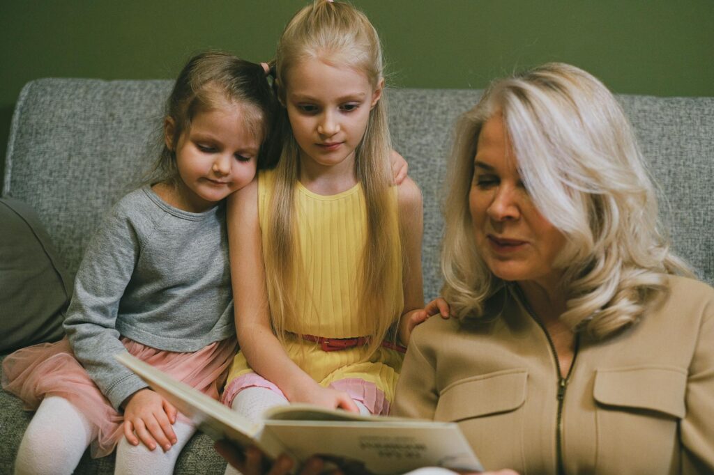 A joyful scene of grandparents reading a story to their grandchildren in a cozy living room. — benefits of grandparents …